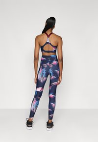Több színű sportos szett, sötét háttérrel és világos virágmintákkal. A felső részen kivágás található, a leggings pedig magas derekú.