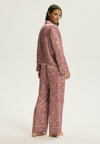 Różowy satynowy komplet piżamowy składający się z bluzki z długim rękawem i spodni o szerokich nogawkach, ozdobiony złotym wzorem kwiatowym. Gładka faktura, dopasowany krój.