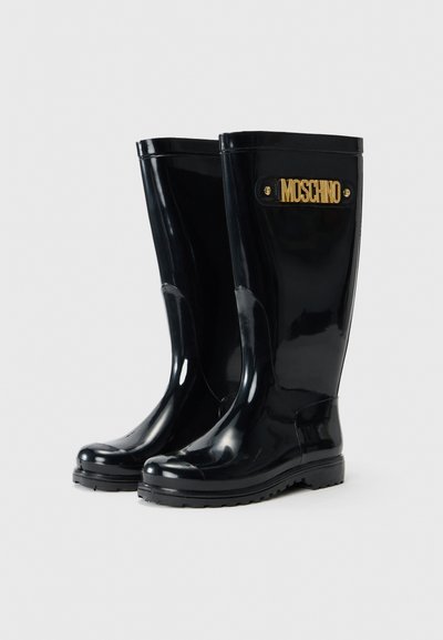 Black rubber rain boots with a glossy finish, featuring a front strap with a gold Moschino logo and a sturdy sole for traction.