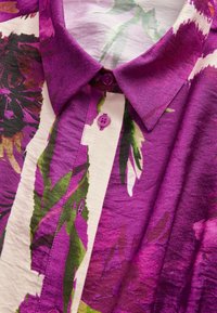 Bluză florală mov cu guler, închidere cu nasturi și un material fin, texturat, cu accente verzi și mauve.