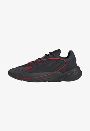 Czarny i ciemnoczerwony sportowy sneaker z wiązaniem na sznurówki, fakturowaną podeszwą i smukłą sylwetką.