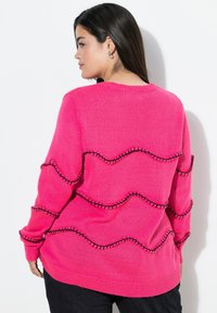 Suéter rosa con un corte relajado, cuello acanalado y acentos de costura ondulada negra a lo largo del cuerpo y las mangas. Tejido de punto texturizado.