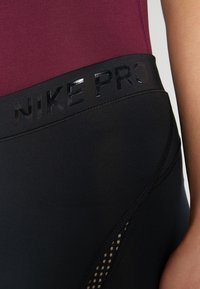 Czarne legginsy sportowe z błyszczącym logo "NIKE PRO" przy pasie. Charakteryzują się gładką fakturą oraz siateczkowym panelem zapewniającym wentylację.