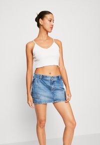 Witte cropped tanktop met golvende randen, gecombineerd met een blauwe denim minirok met een zak en een knoopsluiting. Eenvoudig en casual ontwerp.
