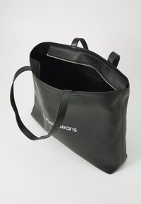 Borsa a spalla nera in pelle con due manici, chiusura con cerniera e testo del logo bianco. Esterno liscio e interno spazioso.