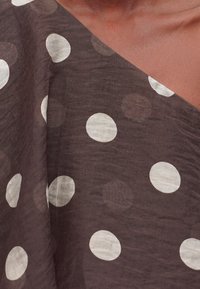 Καφέ ύφασμα με μεγάλα λευκά πουά, μερικώς τοποθετημένο πάνω στον ώμο και το πάνω μέρος του στήθους ενός ατόμου.