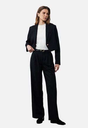 Czarna skórzana marynarka z akcentami złotych guzików, w połączeniu z luźnymi czarnymi spodniami i białym topem z prążkami. Elegancki i minimalistyczny design.