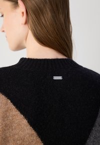 Sweater de malha com um largo colarinho preto, apresentando um design geométrico em preto, bege e cinza. Inclui um detalhe em metal com o logótipo na parte de trás.