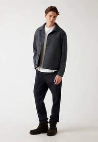 Giacca in misto lana grigia con colletto, chiusura con bottoni e due tasche frontali, abbinata a jeans in denim scuro e stivali neri con lacci.