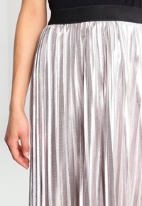 Plisserad kjol med svart resårmidja, tillverkad av glänsande ljusrosa material. Vertikala ränder skapar en strukturerad yta.