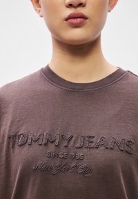 Brun bomuld t-shirt med et broderet logo, der lyder "TOMMY JEANS" og "New York City" i en kontrasterende lysere tråd. Rund hals.