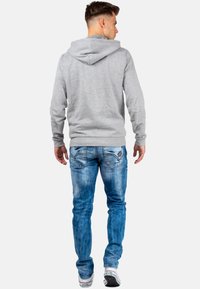 Sweatshirt à capuche gris avec une coupe décontractée, associé à un jean bleu clair avec un délavage et des détails usés. Baskets blanches.