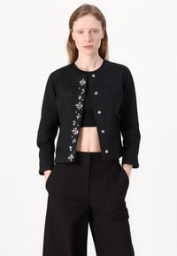 Giacca nera corta con maniche lunghe, caratterizzata da un design floreale in paillettes sul davanti, chiusura con bottoni e due tasche sul petto.