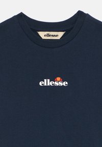 Mörkblå bomullströja med rund hals. Har en vit "ellesse"-logotyp med en röd och orange accent ovanför. Slät textur.