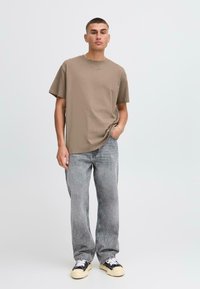 Camiseta oversized color marrón claro con mangas cortas, combinada con jeans de pierna ancha en gris deslavado y zapatillas negras con acentos en crema.