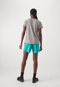 Sportovní oblečení skládající se ze šedého trička s krátkým rukávem a tyrkysových kraťasů. Model nosí černé tenisky a černé ponožky po kotníky.