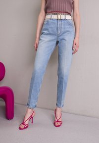 Ljusblå högmidjade jeans med rak ben, kombinerade med ett vitt bälte med ett guldspänne. Matchat med rosa remsandaler med hög klack.