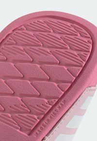 Rosa gummiyttersida med ett texturerat fiskbenmönster; slät övre kant med en kontrasterande vit randdetalj.