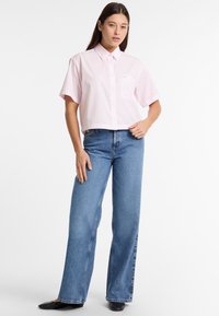Cameria corta a righe rosa con maniche corte e taschino, abbinata a jeans a gamba larga di colore azzurro chiaro. Le ballerine nere completano l'outfit.