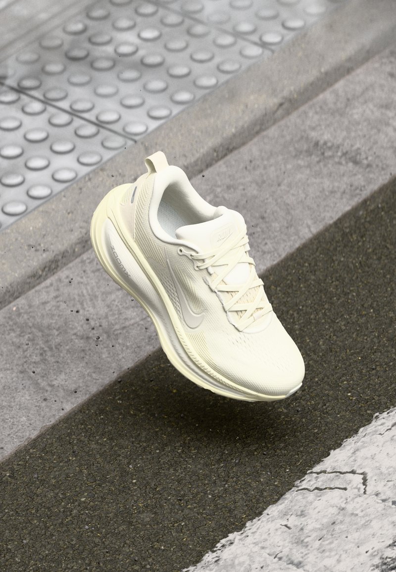 Scarpa da corsa bianca con tomaia testurizzata, pannelli in mesh, lacci e suola ammortizzata. Presenta un accento riflettente e una leggera curvatura.