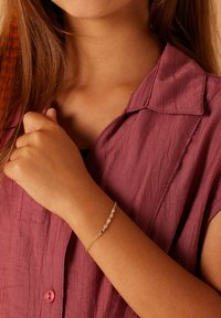 Gouden armband met kleurrijke, gefacetteerde edelstenen in een delicate kettingontwerp, gedragen om een pols. De achtergrond heeft een gestructureerde stof.