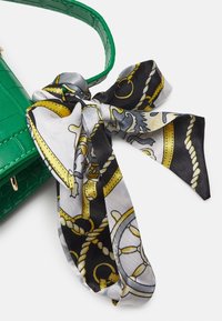 Borsa verde con texture a croco, adornata con una sciarpa in seta bianca e nera legata a fiocco, con dettagli dorati e design elaborati.