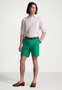 Ανοιχτό ροζ πουκάμισο με ρίγες και κουμπιά, πράσινες σορτς, καφέ δερμάτινη ζώνη και καφέ μοκασίνια. Στενή εφαρμογή, κοντά μανίκια, καθημερινό καλοκαιρινό ντύσιμο.