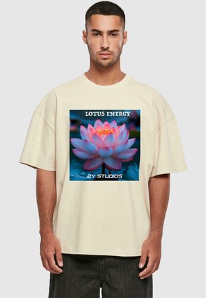 Beige oversized t-shirt featuring a colorful graphic of a pink lotus flower with "LOTUS ENERGY" and "2Y STUDIOS" text at the bottom.