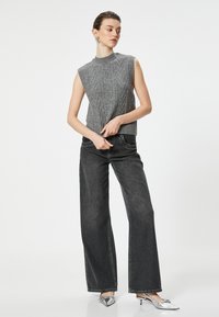 Helles graues, gestricktes ärmelloses Oberteil mit strukturiertem Muster, kombiniert mit hochtaillierten schwarzen weit geschnittenen Jeans und silbernen spitzen Pumps.