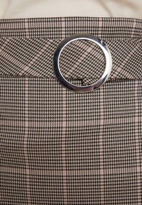 Jupe taille haute avec motif pied-de-poule beige et noir, avec ceinture en tissu assortie et grande boucle circulaire argentée brillante.