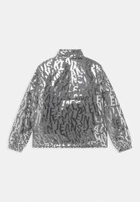 Veste argentée transparente avec un motif de texte noir répété. Équipée de poignets élastiques et d'un col, texture lisse.