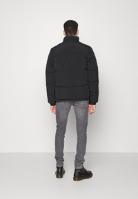 Giacca a vento nera con colletto alto, caratterizzata da sezioni trapuntate orizzontali. Indossata sopra jeans skinny grigi e stivali neri con lacci.