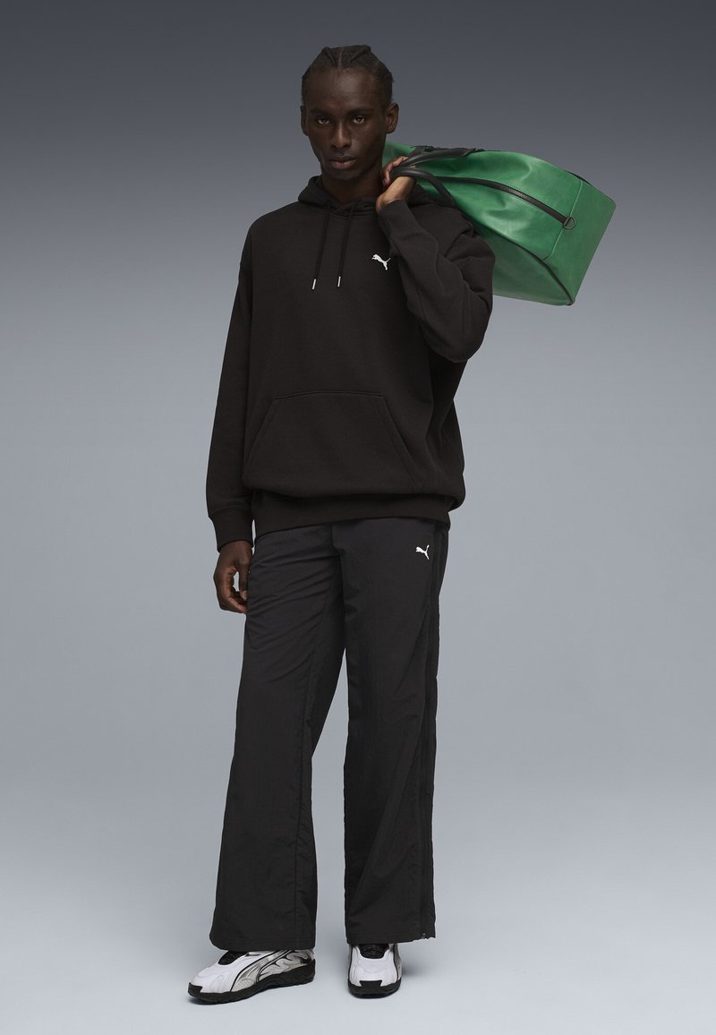 Sudadera negra con bolsillo canguro y logo blanco, combinada con pantalones deportivos negros. Bolsa de deporte verde con doble asa. Zapatillas negras y blancas.