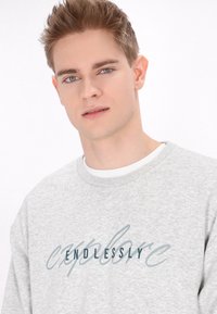 Felpa grigia con collo rotondo e testo "ENDLESSLY EXPLORE" in blu. Realizzata in tessuto morbido, presenta una vestibilità casual e maniche con polsini standard.