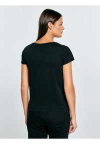 Czarny krótki top z miękkiego materiału, z okrągłym dekoltem i luźnym krojem. W połączeniu z czarnymi spodniami, podkreślającymi prostotę.