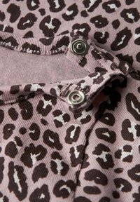 Tissu rose clair avec un motif léopard en marron foncé. Comprend des fixations à pression en métal argenté et un détail de bord texturé et côtelé.