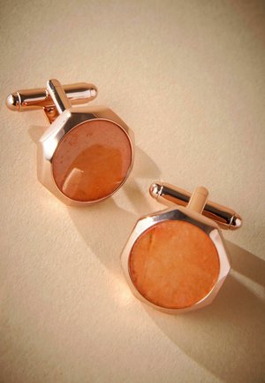 Rose gold cufflinks feature octagonal shapes with orange stone inlays, polished surface, and rounded accents. Displayed on a light beige background.