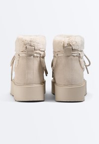 Paire de bottes d'hiver en daim beige avec bordure en fourrure, semelles épaisses et lacets, vues de dos sur fond blanc.