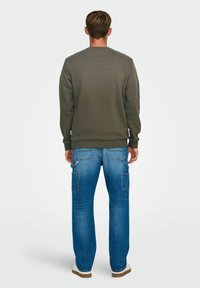Olivengrüner Sweatshirt mit Rundhalsausschnitt, kombiniert mit blauen Jeans-Cargohosen, die mehrere Taschen und eine gerade Passform haben.