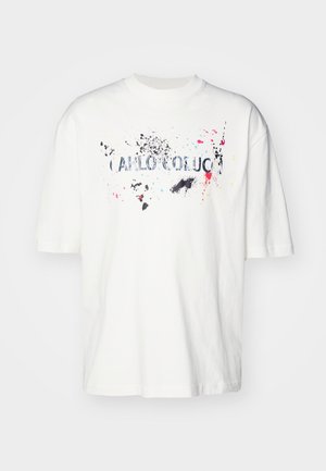 White cotton t-shirt with short sleeves, featuring a colorful splatter design and text "CARLOCOBUCC" in blue across the front.