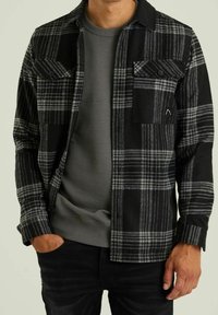 Černá a šedá kostkovaná flanelová košile s knoflíkovými kapsami, nošená přes šedou ribbed dlouhý rukáv, s volným střihem a měkkou texturou.