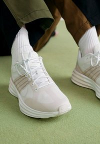 Scarpe da atletica leggere di colore bianco con accenti beige, dotate di una tomaia in mesh traspirante, suola imbottita e sistema di allacciatura prominente.