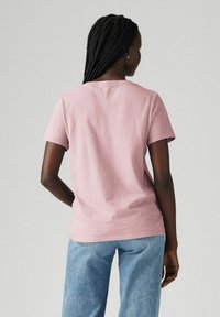 Różowa bawełniana koszulka z krótkim rękawem, okrągłym dekoltem i luźnym fasonem, w połączeniu ze jasnoniebieskimi dżinsami. Prosty i minimalistyczny design.