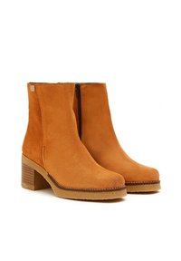 Botines de ante color marrón claro con tacón bloque, cremallera lateral y detalles de costura a lo largo de la suela. Textura suave con un acabado mate.
