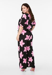 Salopette nera a gamba larga con motivo floreale rosa, maniche corte, vita elasticizzata e sofisticati tacchi rosa; tessuto liscio, vestibilità rilassata.