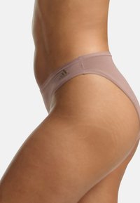 Bikini mauve clair avec une texture lisse et un design minimaliste, doté d'une fine ceinture et d'un logo discret sur le côté.