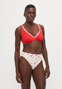 Rød ribbet bikinioverdel med hvit kant, kombinert med høyt liv hvite bunn med et fargerikt fruktmønster. Glatt stoff, tettsittende design.