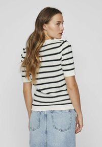 Top de punto a rayas en blanco y negro con mangas cortas y escote redondo. El material texturizado cuenta con un dobladillo acanalado y un diseño estructurado.
