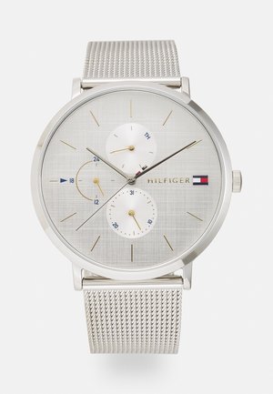 Montre-bracelet Tommy Hilfiger argentée avec bracelet en maille, cadran minimaliste, index des heures dorés, et trois sous-cadrans pour le jour, la date et l'heure sur 24 heures.