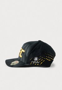 Μαύρο καπέλο με σχεδιασμό μοτίβου, με κεντημένο κίτρινο λογότυπο και διακοσμητικά στοιχεία. Περιλαμβάνει ετικέτα λογότυπου με την ένδειξη "crypto.com" στο πλάι.